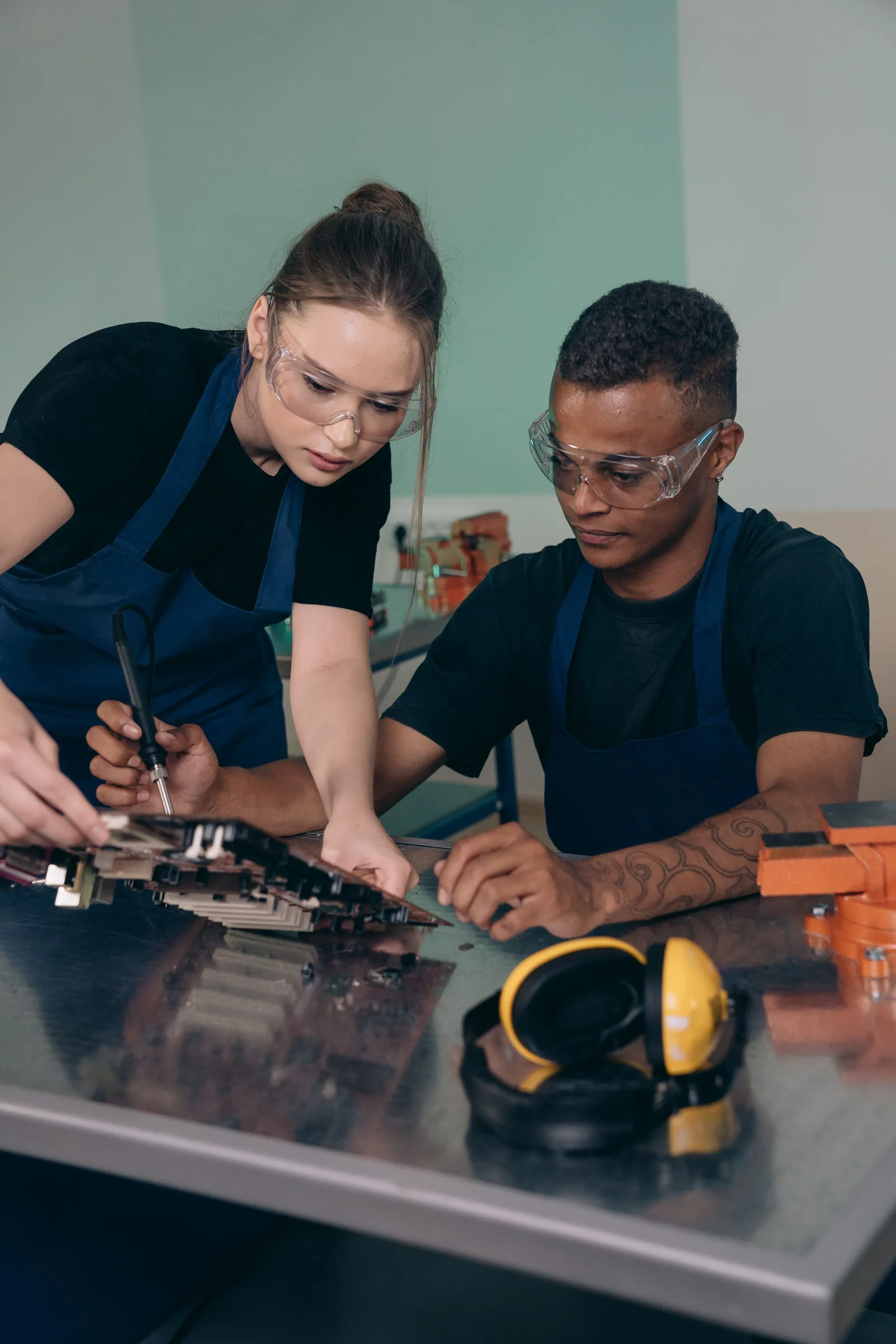 A woman and man collaborate on electronic hardware at a workbench.