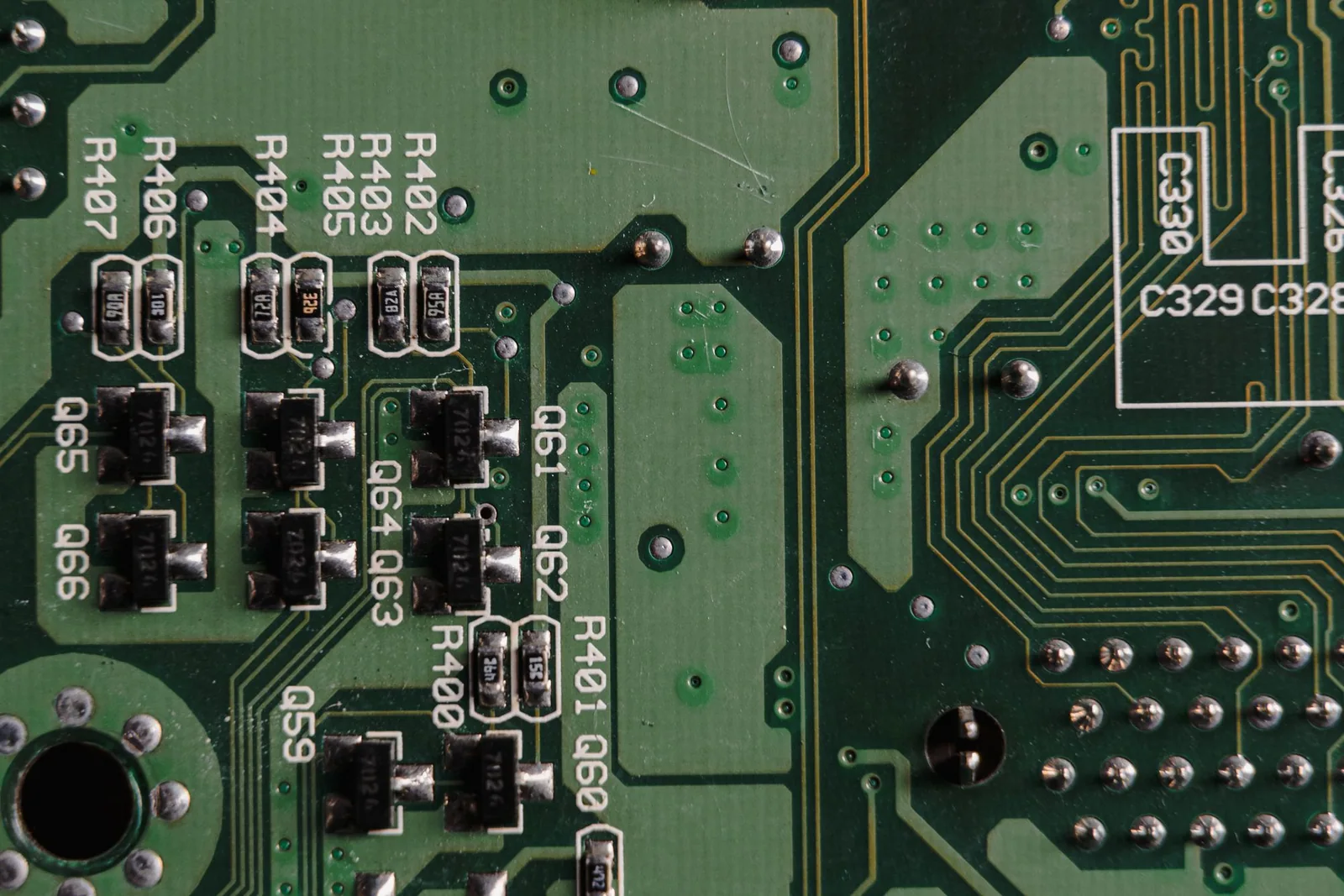 Close-up of a green printed circuit board with labeled electronic components, solder joints and fine connecting traces.
