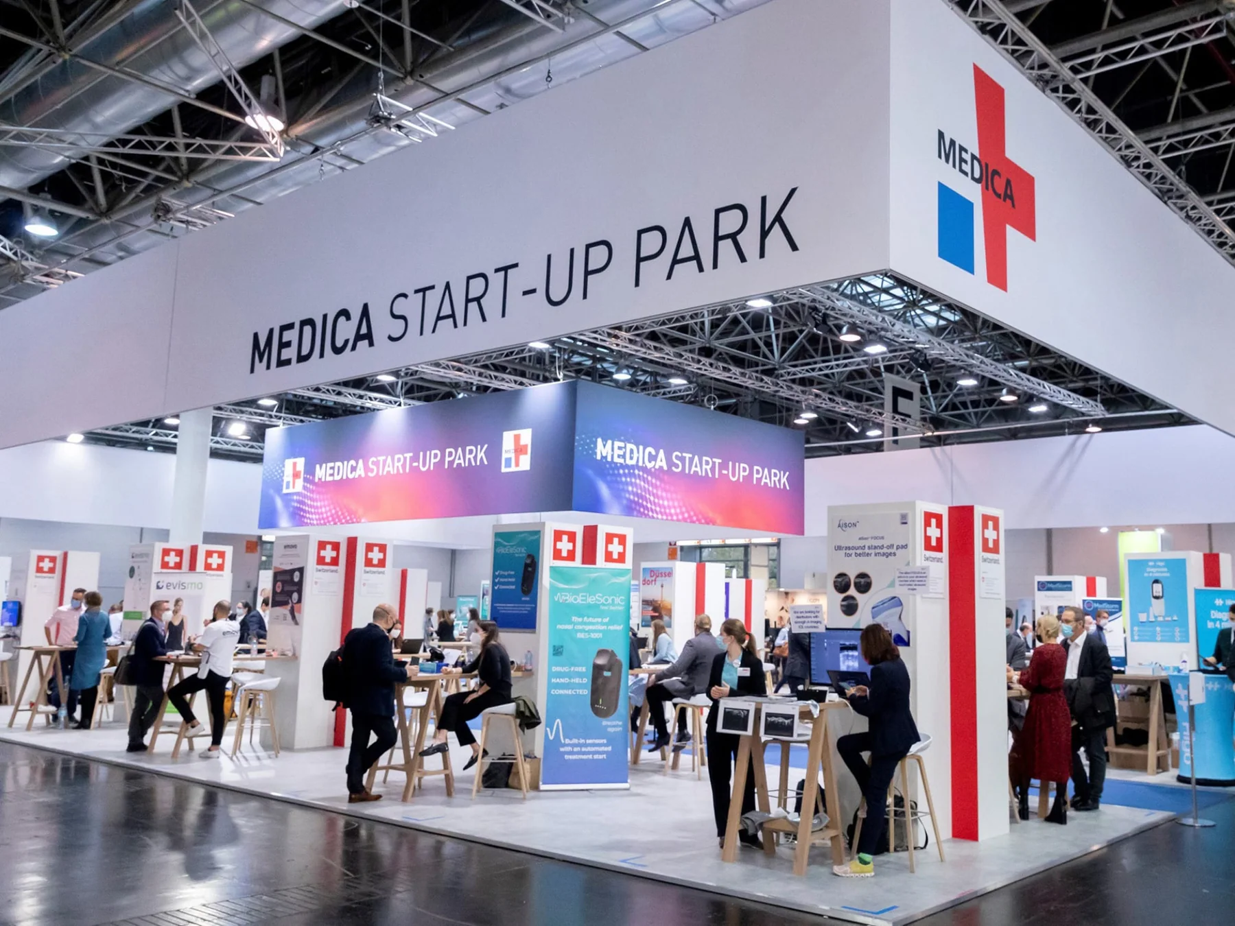 Medical exhibitors and visitors meeting beneath the illuminated start-up pavilion at MEDICA Düsseldorf 2021.