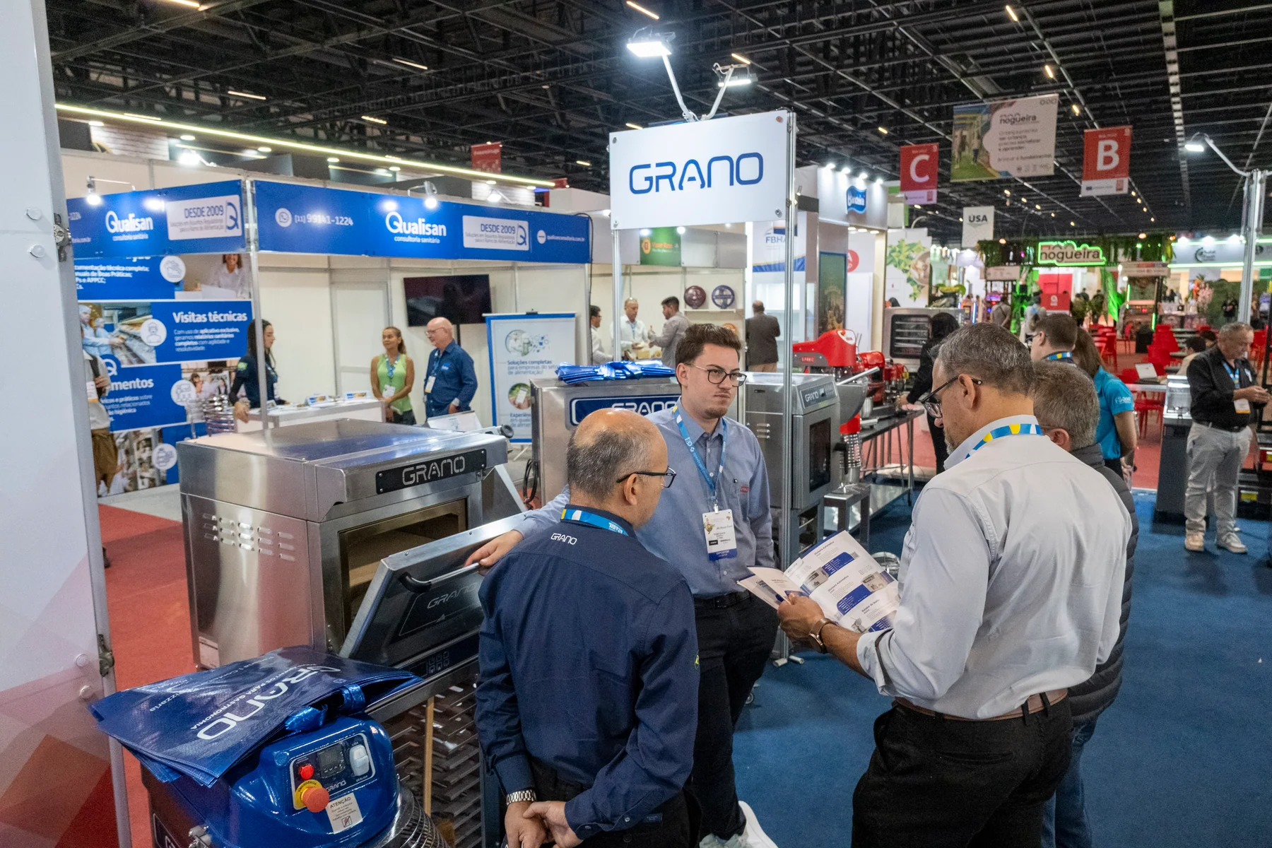 Food-industry exhibitors discussing equipment with visitors among busy booths at Anuga Select Brazil 2025.