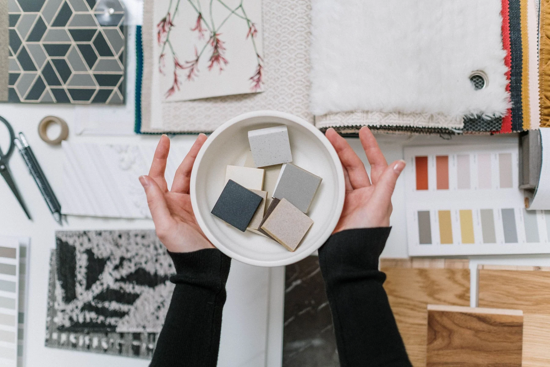 Hands hold small finish samples above a table of geometric tile, textiles and color palettes.