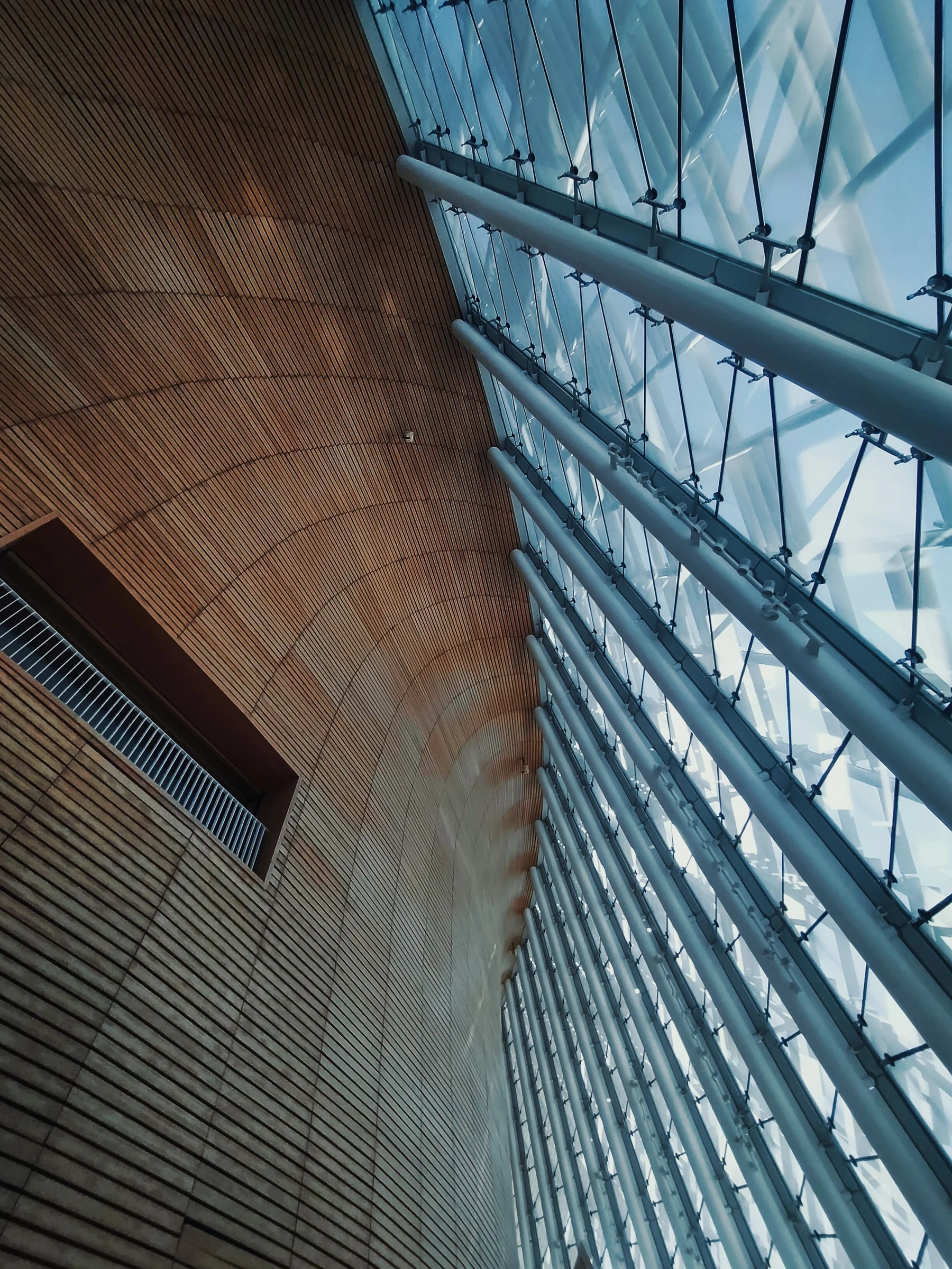 Sculptural timber walls meet a tall glass facade and exposed structural connections inside a modern exhibition center.