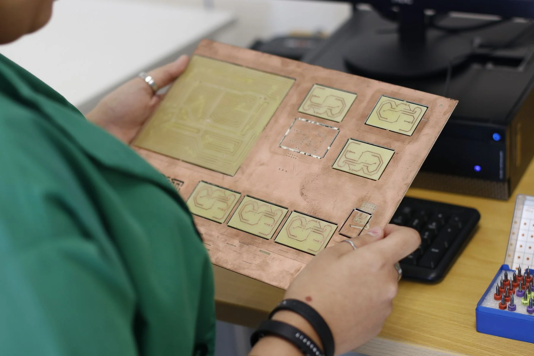 A technician holds a copper board containing several patterned electronic circuit samples.
