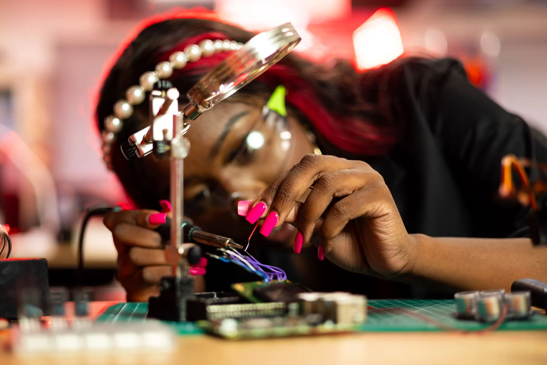 A woman works on circuitry with precision tools beneath a magnifying lens.