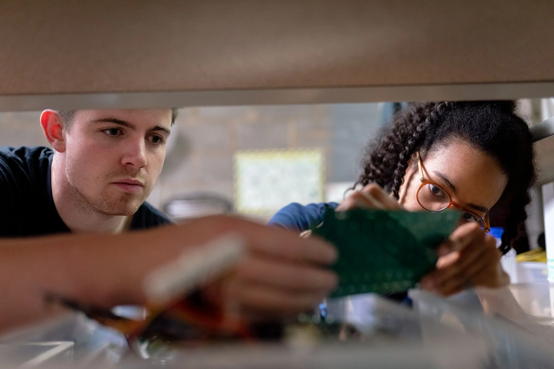 Two engineers examine the same circuit board at an electronics workbench.