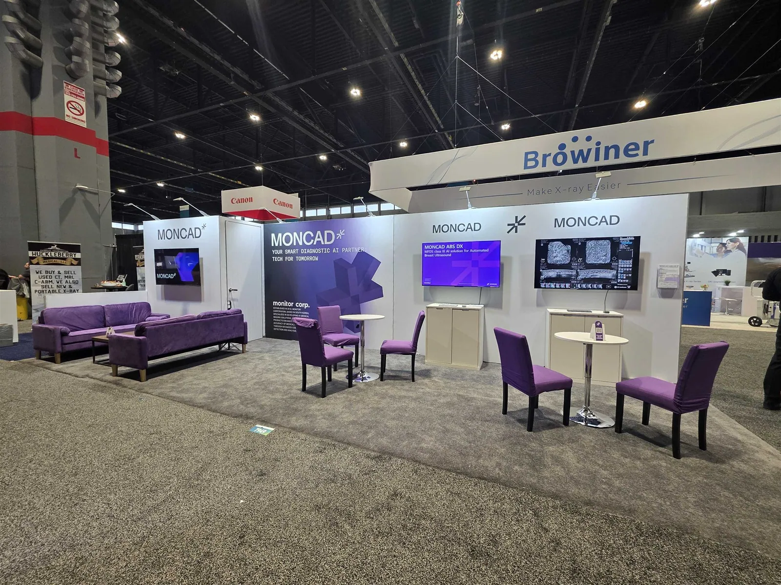 MONCAD medical-imaging exhibit with diagnostic screens, white walls, purple sofas and consultation tables; a Browiner sign hangs beyond it.