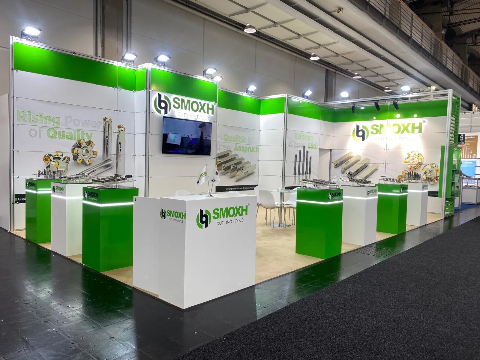 SMOXH exhibit with green-and-white walls, cutting-tool displays, a wall-mounted screen and a small meeting table.