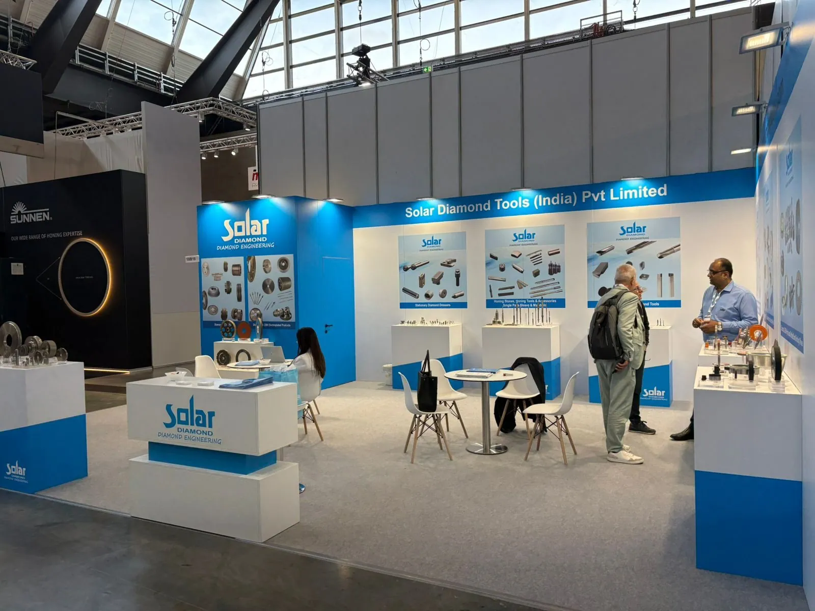 Solar Diamond Tools exhibit with blue-and-white walls, sample plinths, cutting-tool diagrams, meeting chairs and two visitors talking.