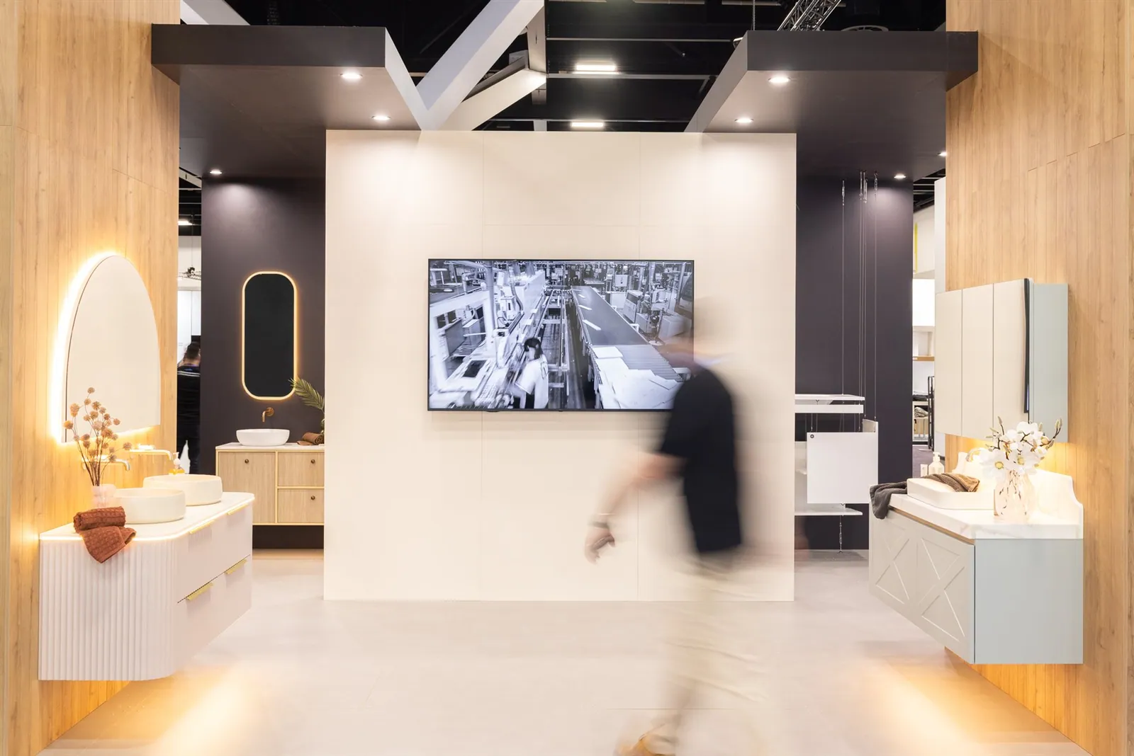 A visitor passing through Timberline’s timber-framed exhibit between illuminated bathroom vanities and a large wall-mounted screen.