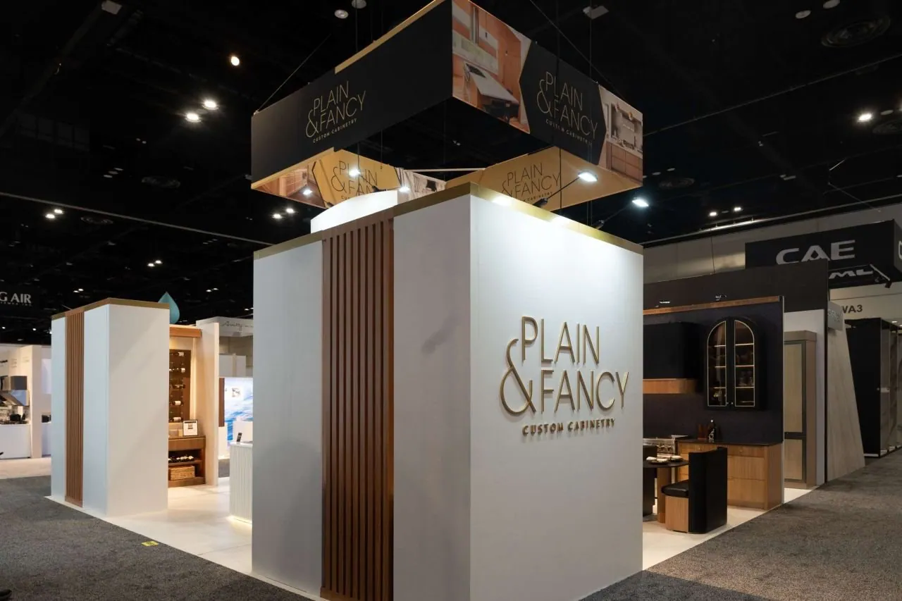 Plain & Fancy custom cabinetry exhibit with a white entrance wall, timber slat panel, illuminated logo and dark cabinet displays.