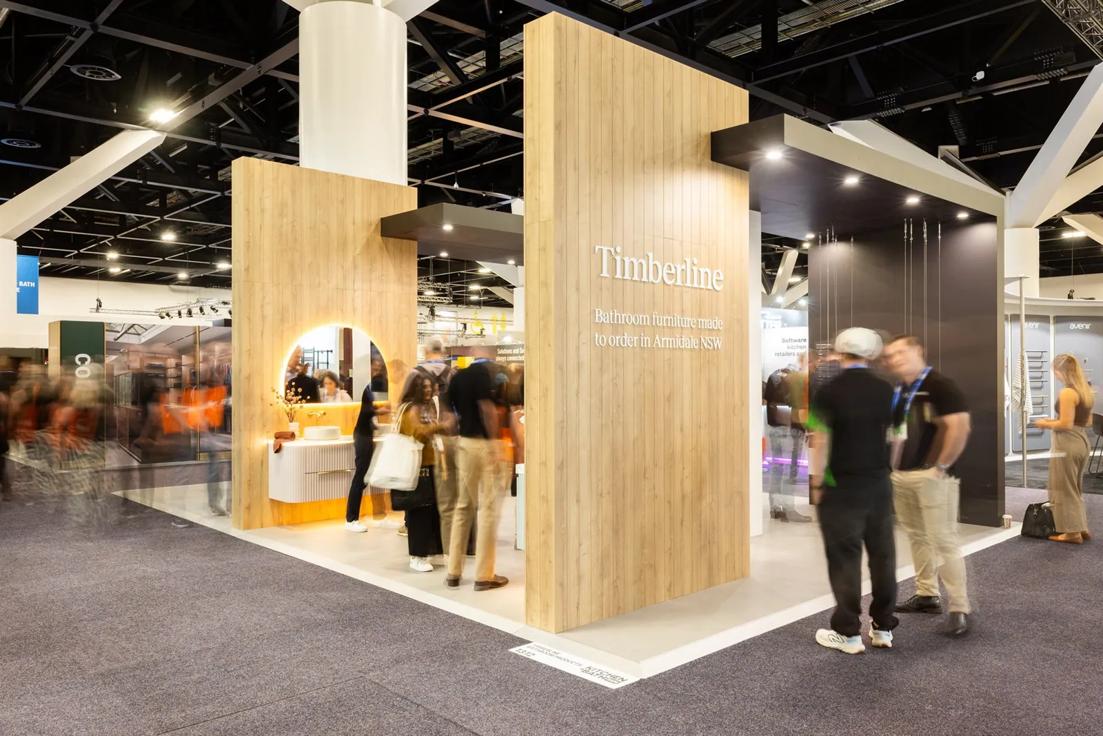 Timberline exhibit with tall timber panels, a black overhead frame, illuminated bathroom vanities and visitors in the aisle.