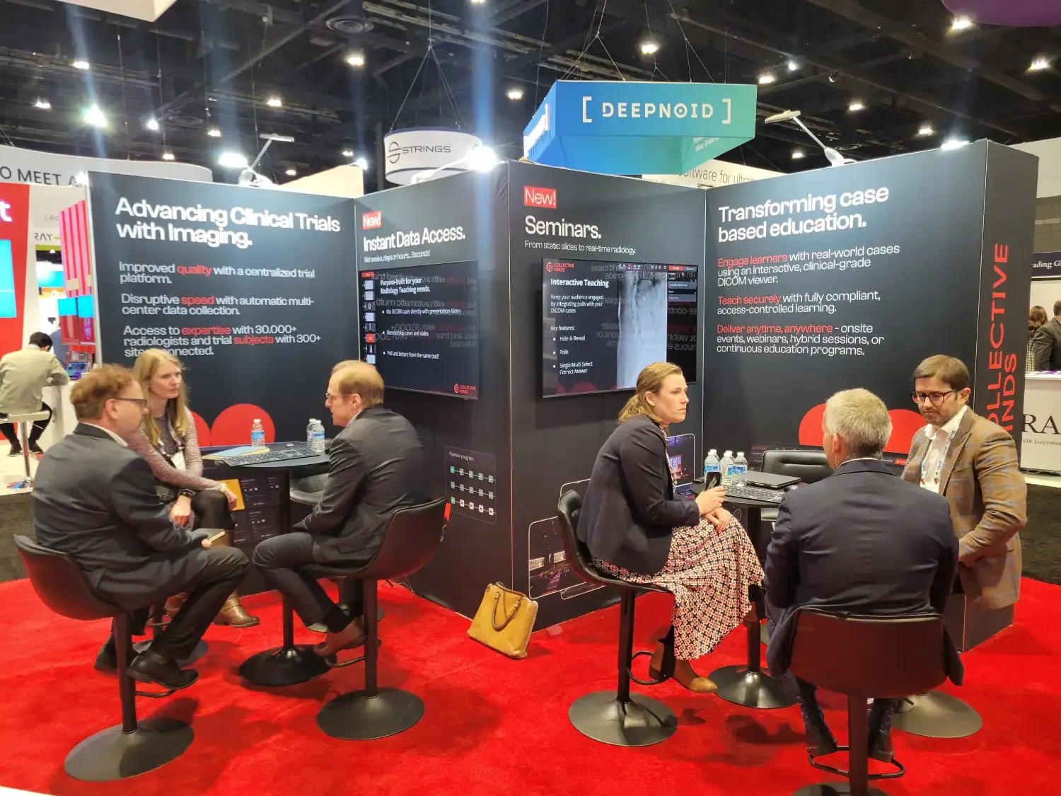 Visitors meeting at two tables in Collective Minds' red-carpeted exhibit, with clinical-trial imaging graphics and software screens.
