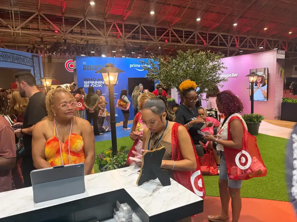 Attendees interacting with a staffed tablet counter inside Amazon’s colorful ESSENCE activation.