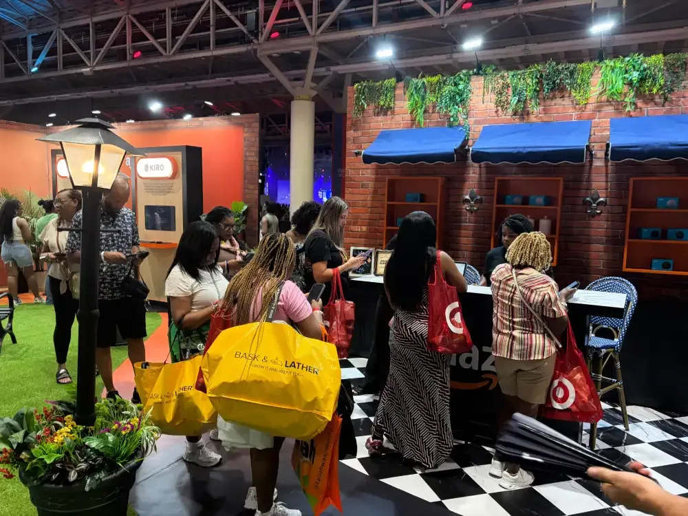 Visitors gathered around a counter in Amazon’s activation, with a brick-style storefront, blue awnings and black-and-white floor pattern.