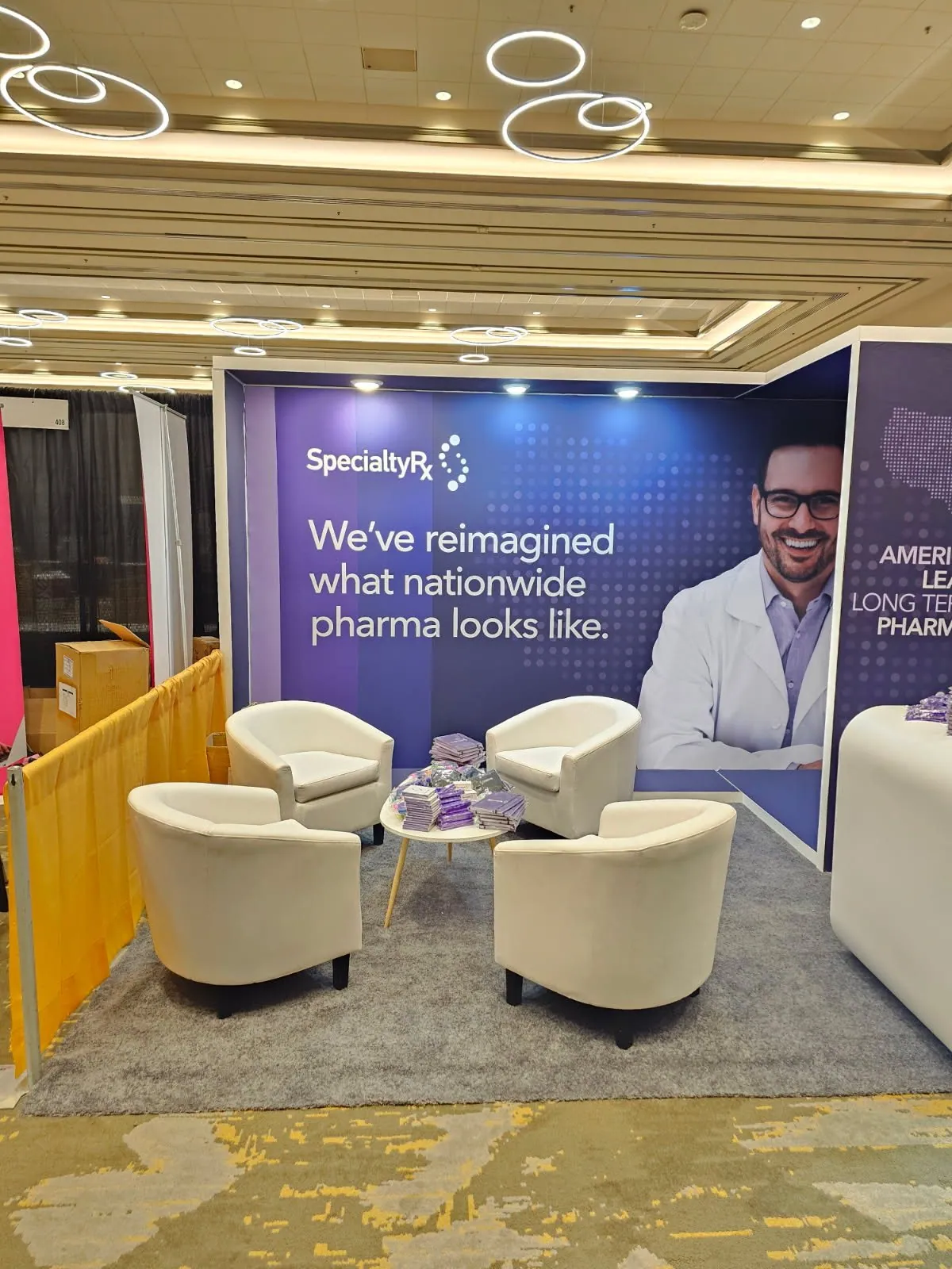 Four white armchairs arranged around a low table inside SpecialtyRx's purple pharmacy exhibit.