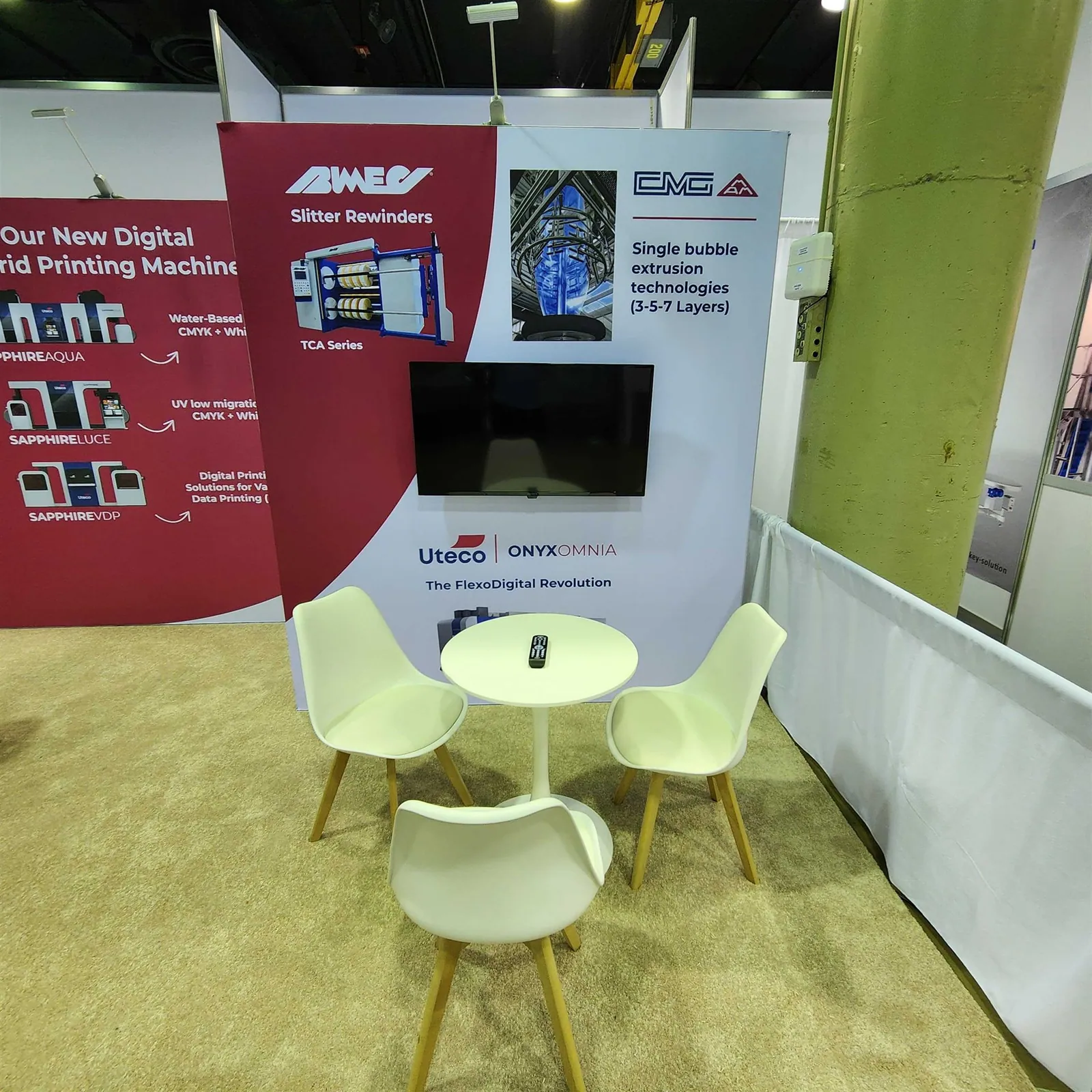 White meeting table beneath a screen and printing-equipment graphics for Uteco, CMG and Bimec in the FlexCA exhibit.