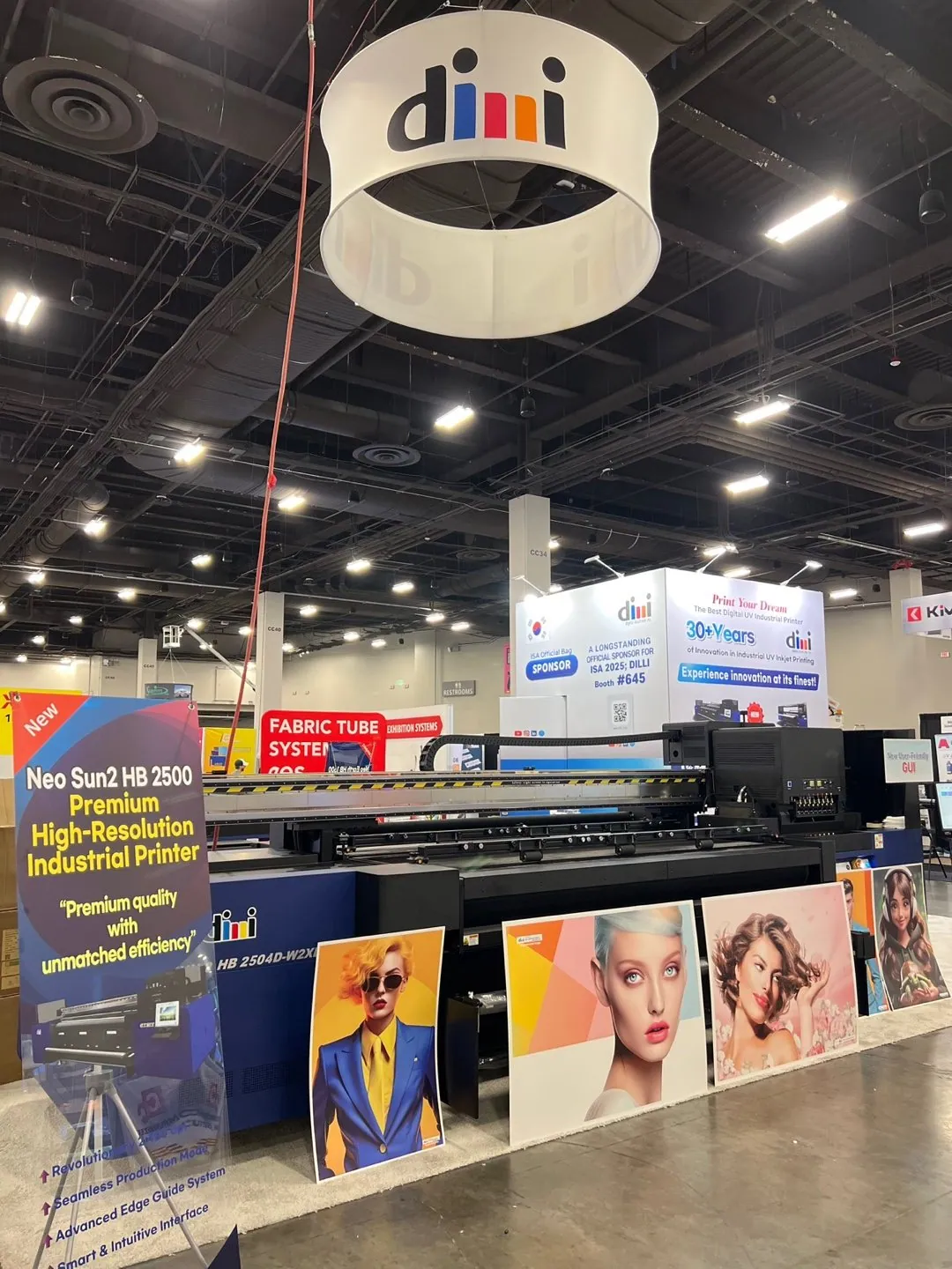 DILLI industrial printer and printed sample panels beneath a circular hanging sign, with booth graphics referencing ISA 2025 and booth 645.