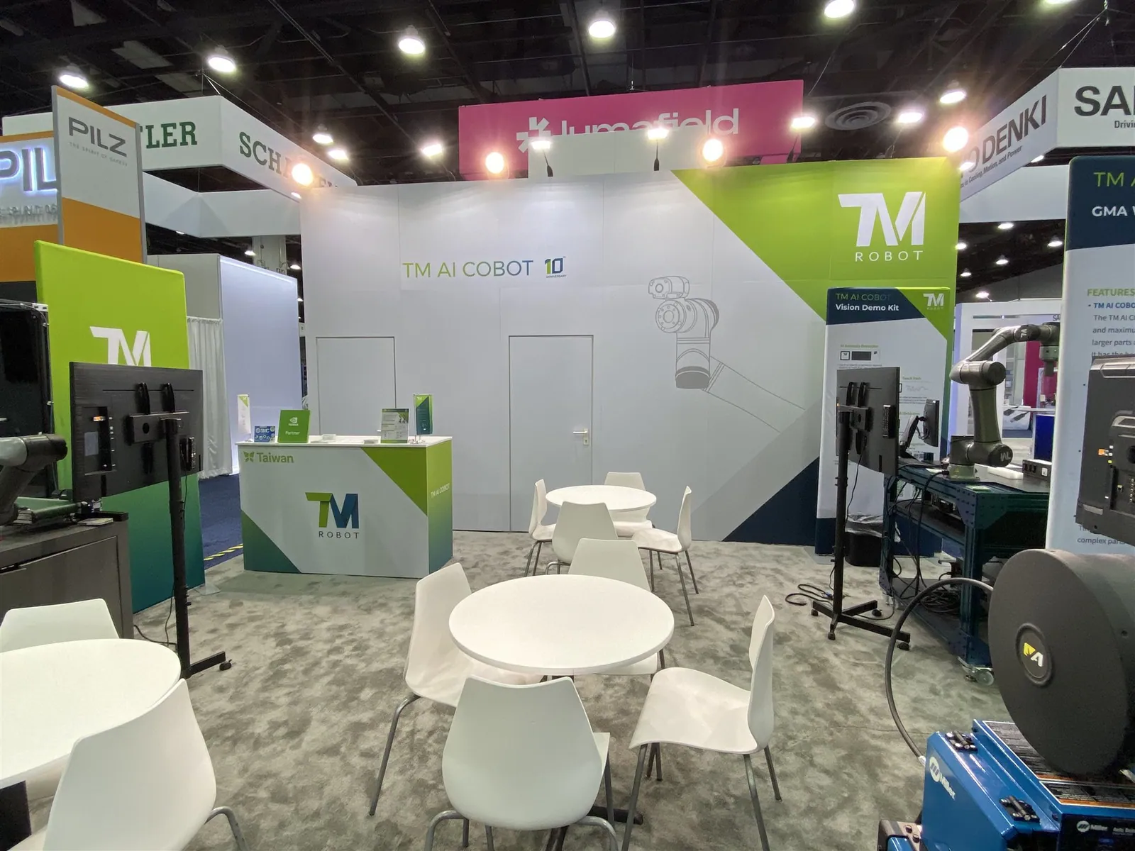 Techman Robot exhibit interior with white meeting tables, a green-and-white reception counter, robotic arms and vision-demonstration screens.