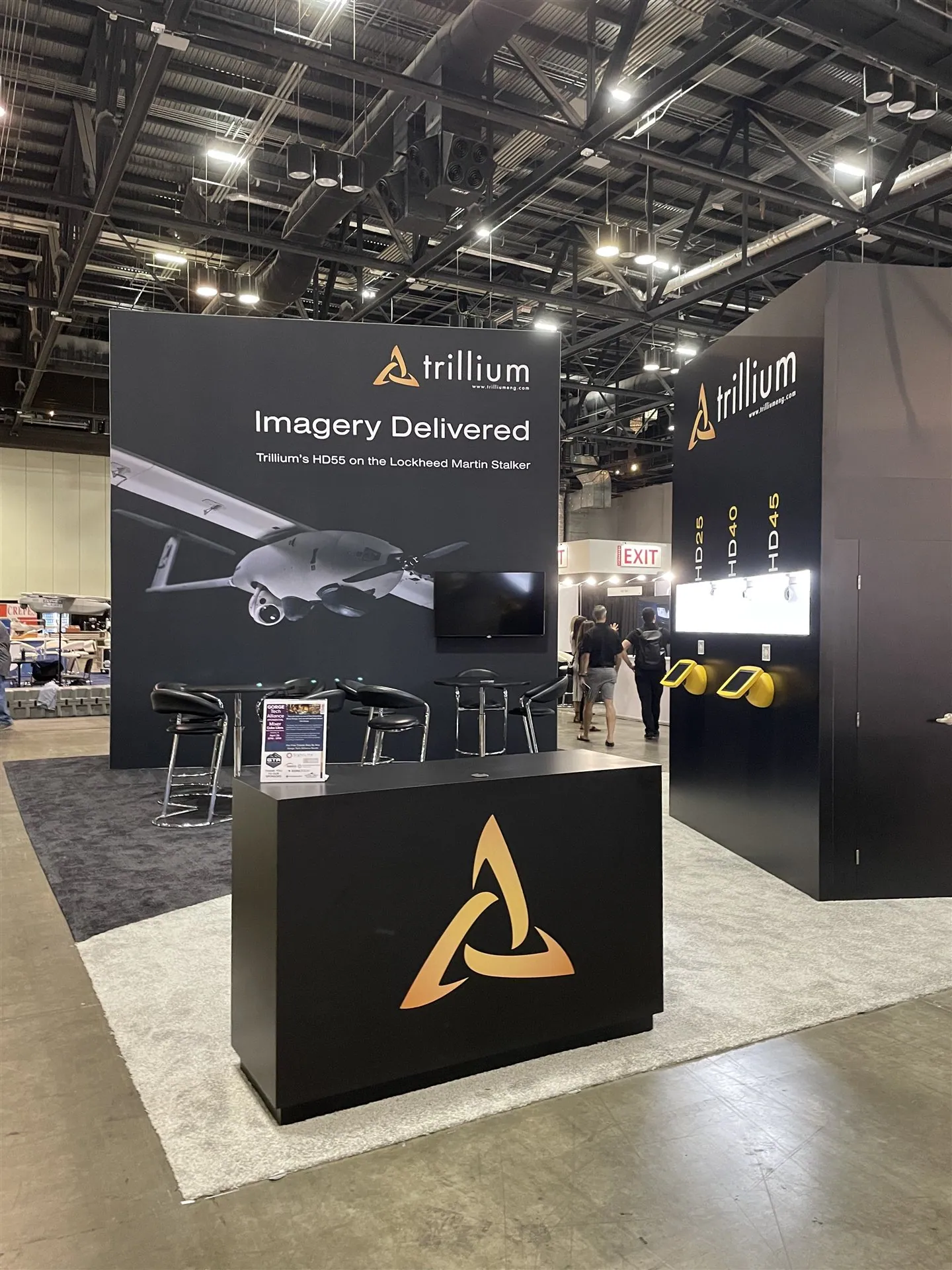 Trillium Engineering reception counter in front of dark aircraft graphics and illuminated imaging-sensor displays.