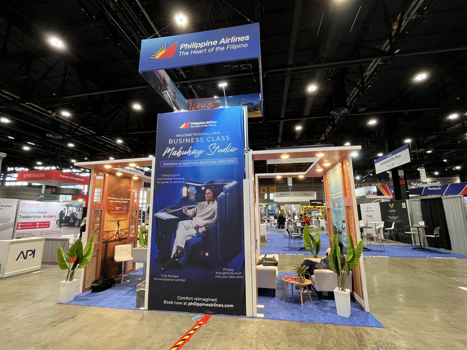 Philippine Airlines exhibit entrance with a blue business-class tower, suspended airline sign, warm rectangular frames and plants.