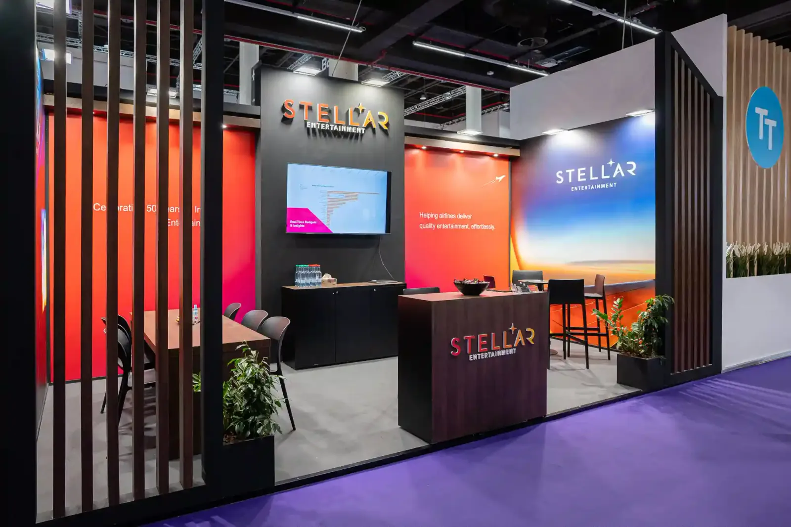 Stellar Entertainment exhibit with orange and blue wall graphics, a presentation screen, reception counter and meeting area framed by dark timber slats.