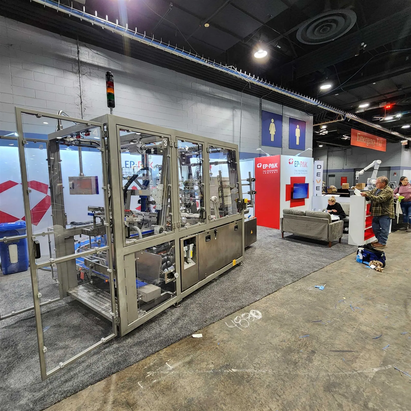 Long enclosed packaging machine in the EP-PAK exhibit with metal framing, a control panel and branded red-and-white walls.