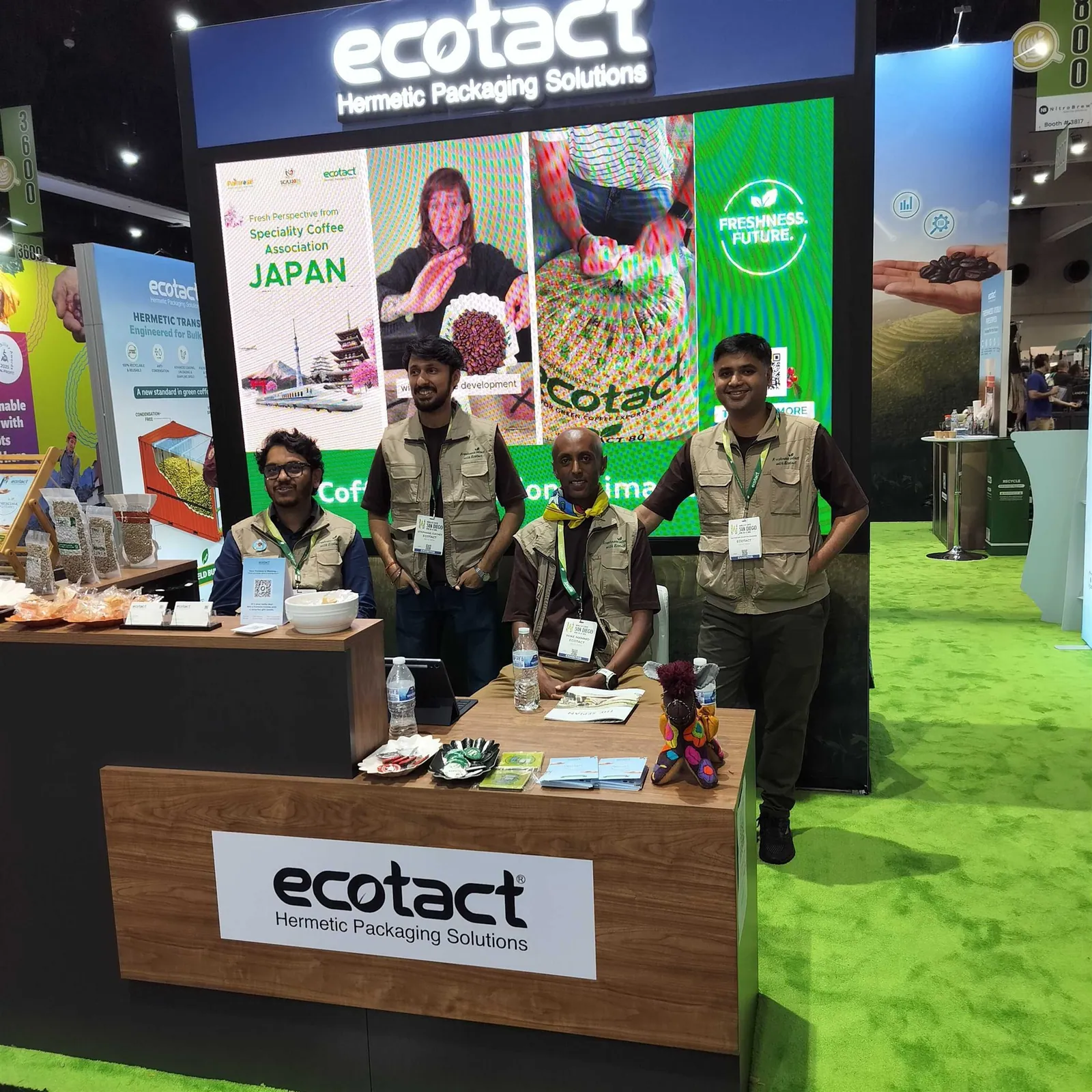 Ecotact team posing behind a branded counter surrounded by packaging samples, product graphics and a large display screen.