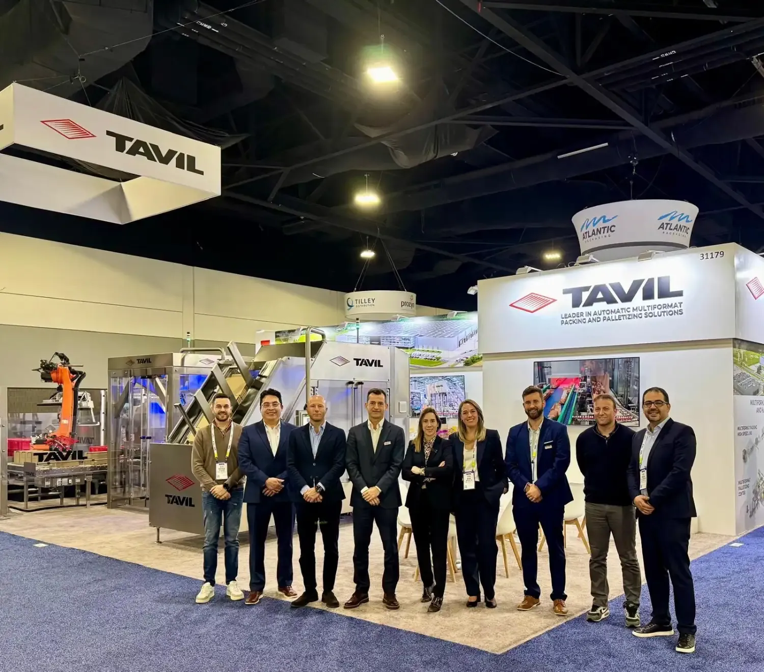 TAVIL team standing in front of an exhibit with suspended branding, a protected machinery area and meeting tables.