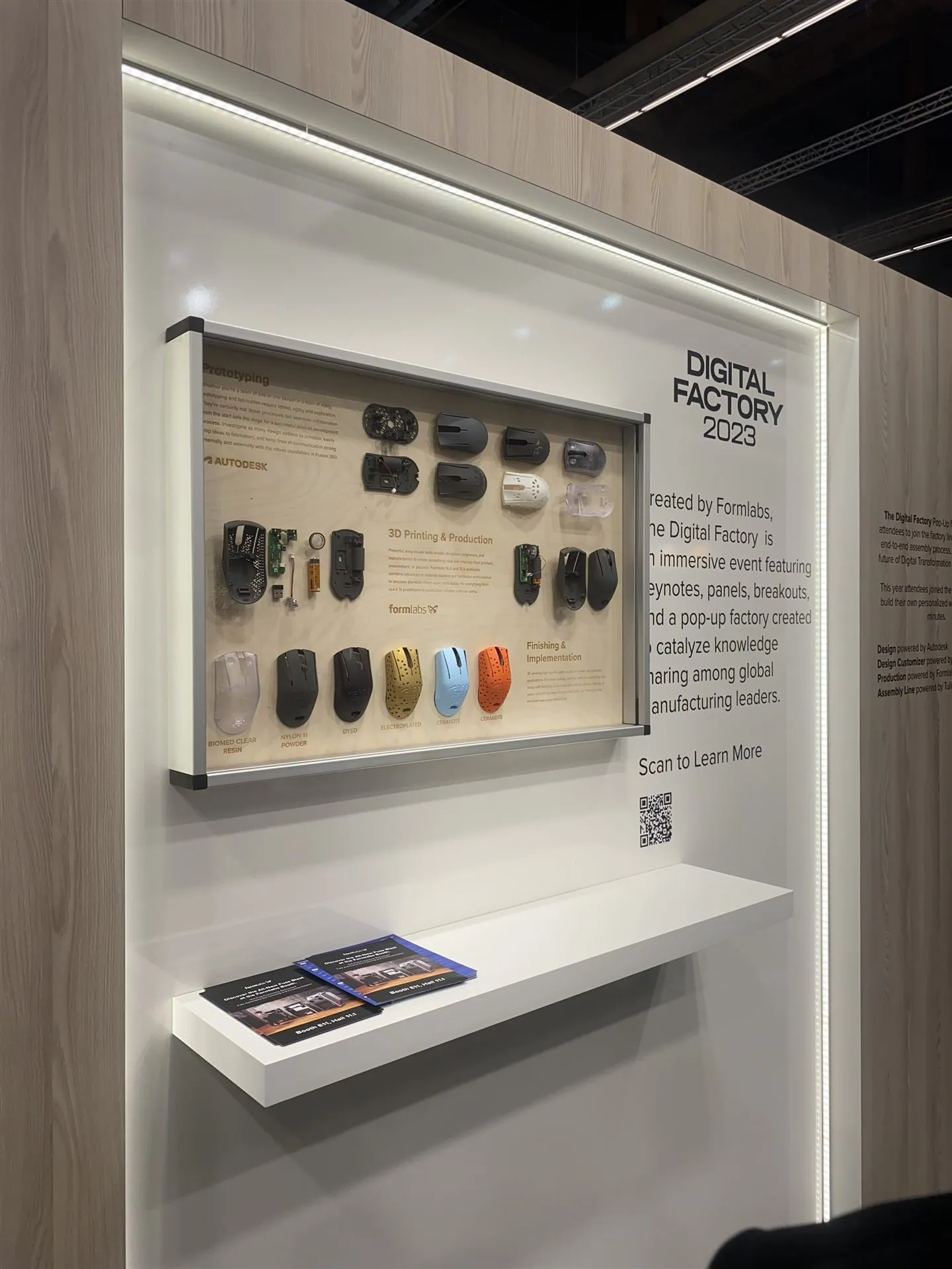 Illuminated Digital Factory display with mouse prototypes, printed shells and finished parts arranged under prototyping, 3D printing and finishing labels.
