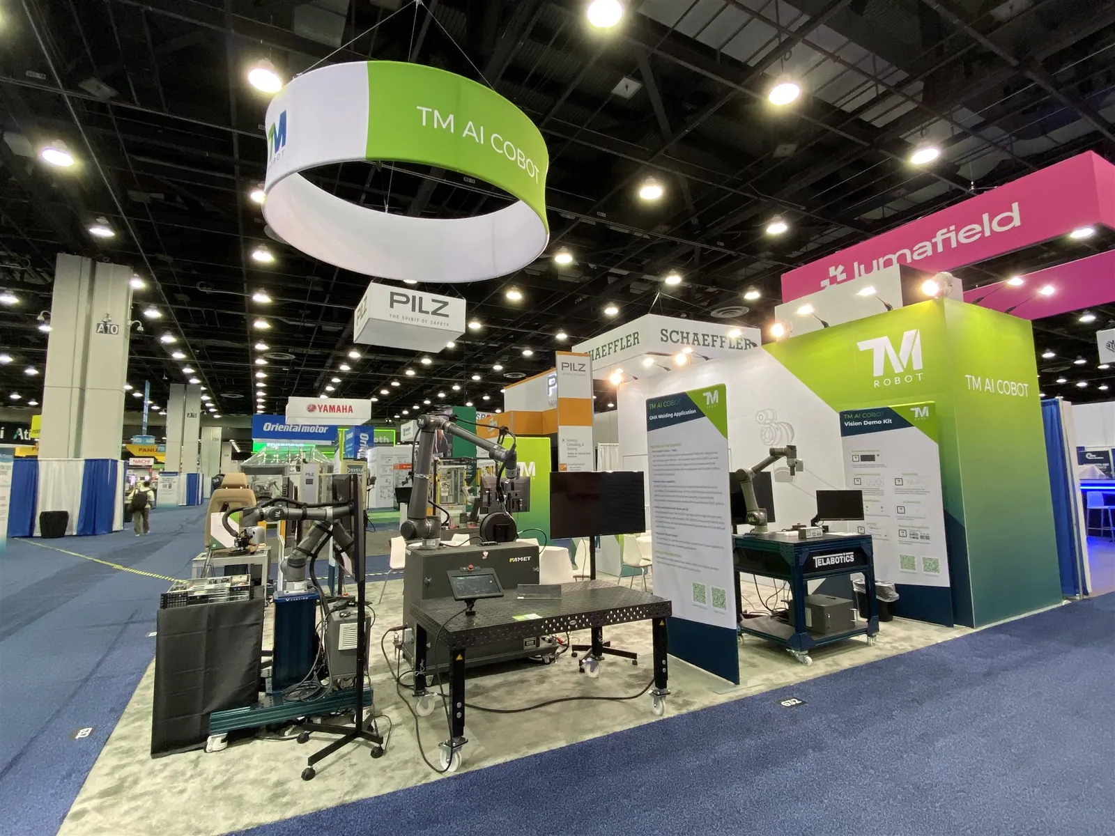 Techman Robot's AI Cobot exhibit with industrial robotic arms, demonstration equipment and a circular overhead brand sign.