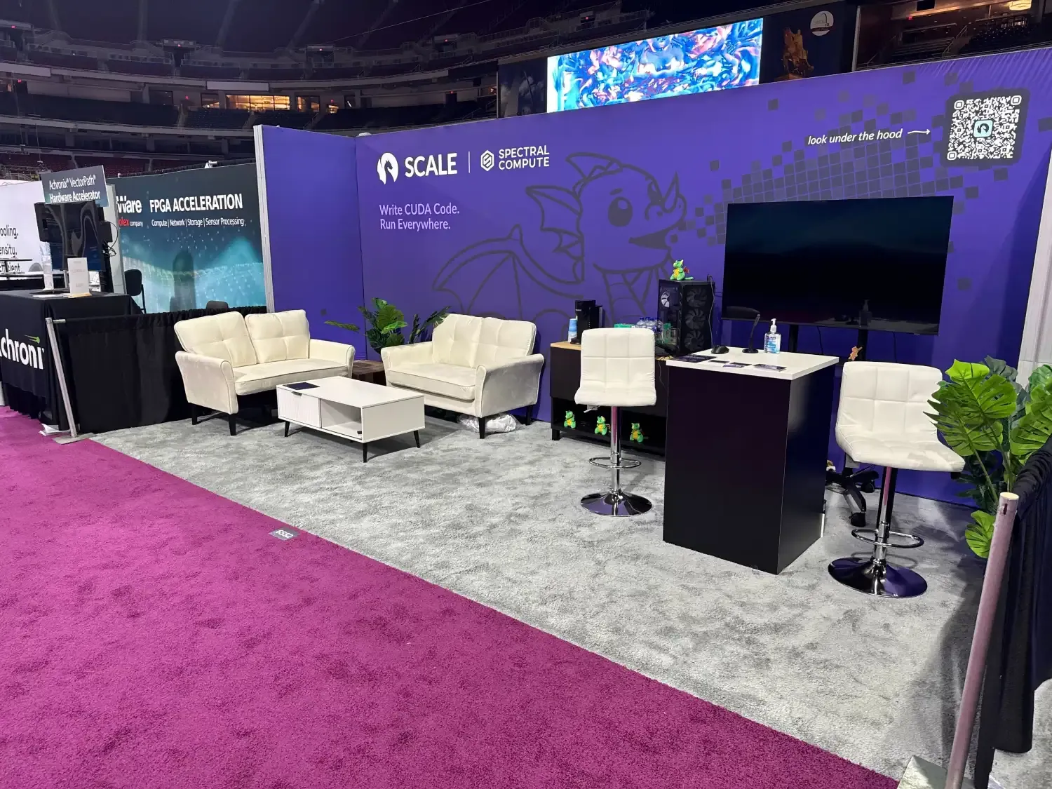 Spectral Compute exhibit with purple SCALE software graphics, white lounge seating, a large screen and a black reception counter.