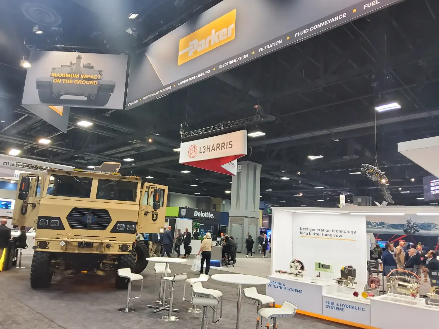 Parker exhibit with a military vehicle beside white meeting tables, fuel and hydraulic component displays and overhead Parker branding.