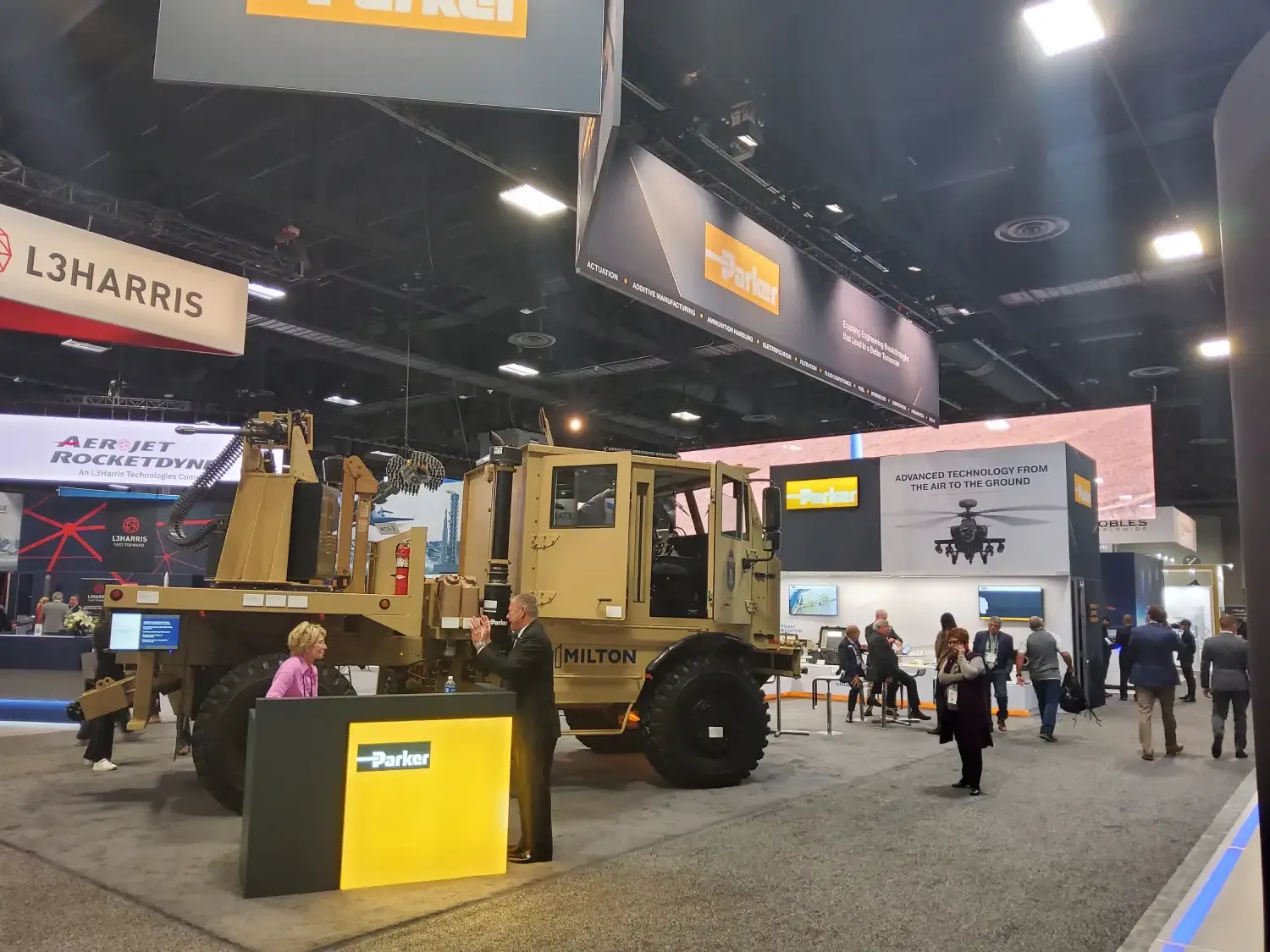 Parker defense exhibit with a military vehicle, large suspended brand signs, illuminated reception counter and visitors beside technical product displays.