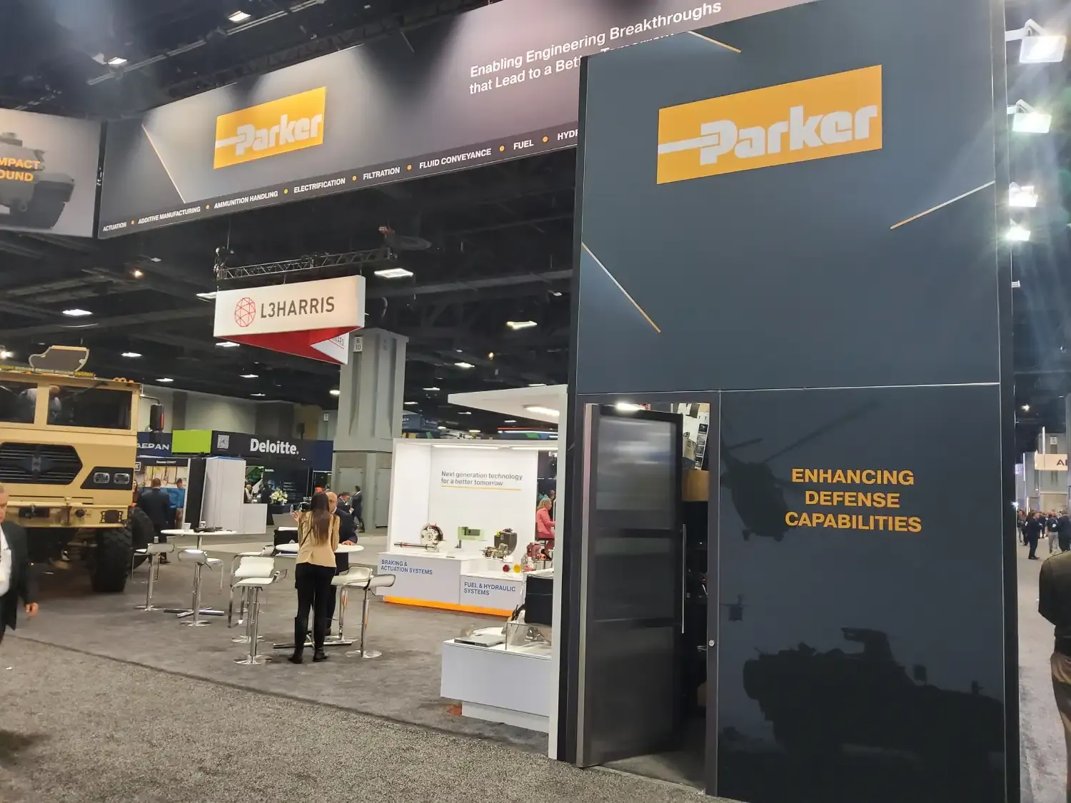 Tall Parker exhibit tower carrying an Enhancing Defense Capabilities message beside component displays and open meeting tables.