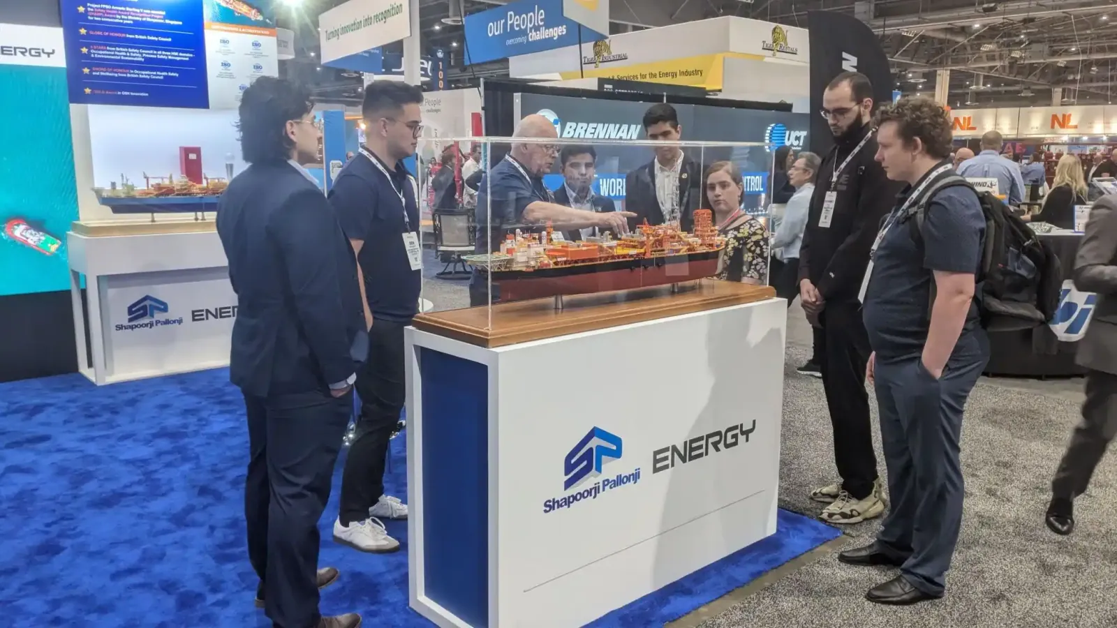 Visitors discussing a detailed vessel model on Shapoorji Pallonji Energy’s branded white display counter.