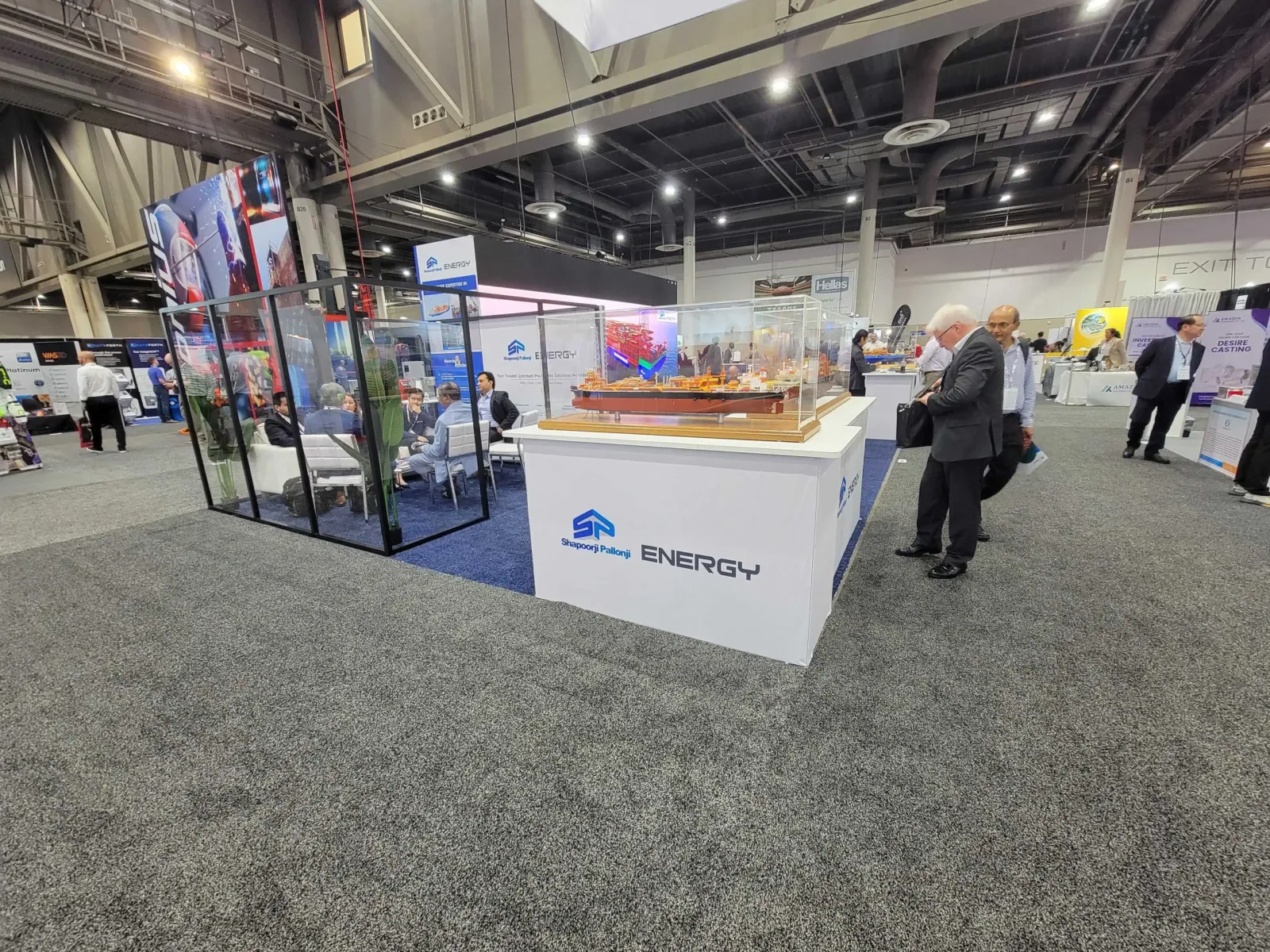 Shapoorji Pallonji Energy exhibit with a glass meeting room and a detailed vessel model in a transparent case on an illuminated white counter.