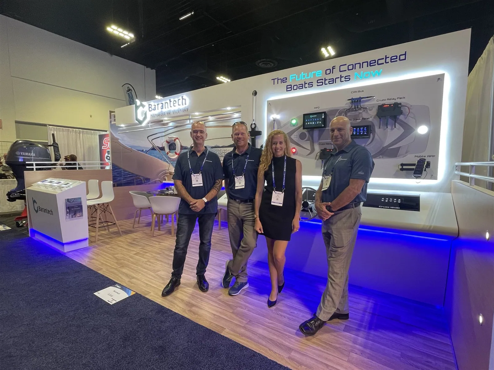 Four people standing in Barantech’s marine-controls exhibit beside an illuminated connected-boat systems wall and blue-lit demonstration counter.