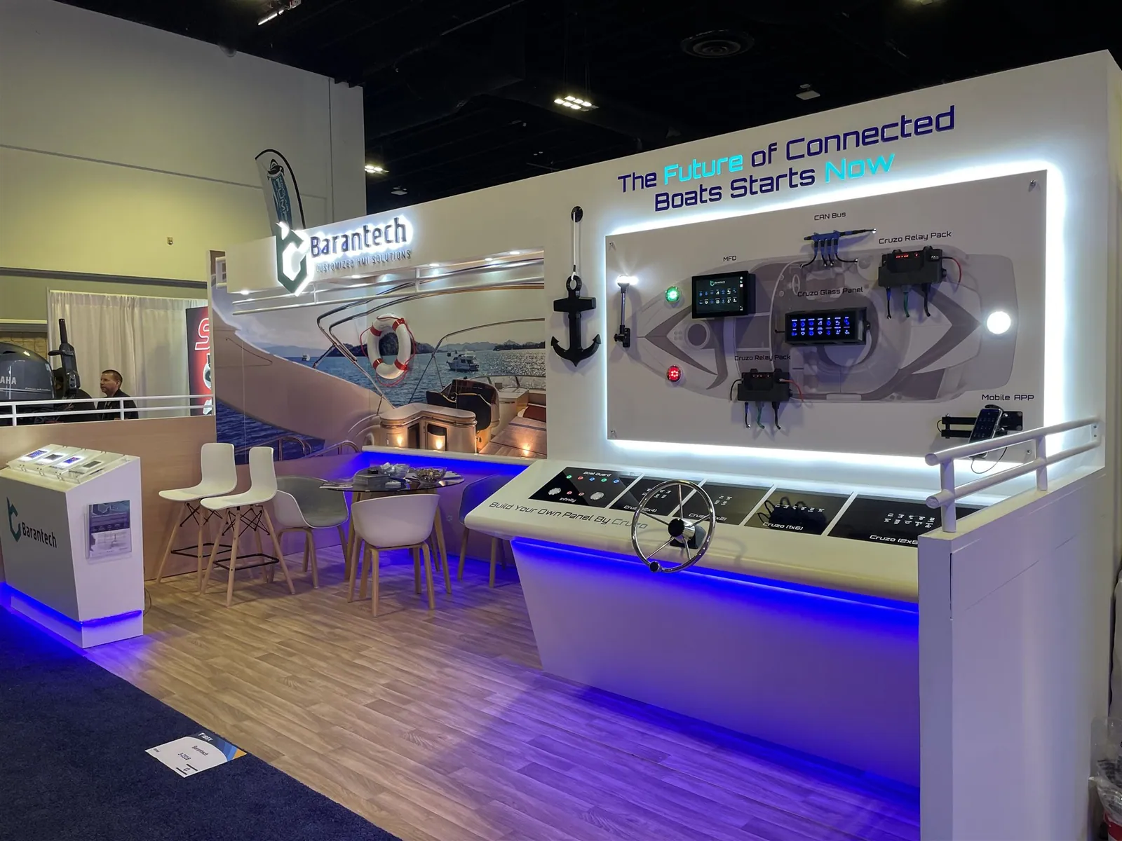 Barantech connected-boat exhibit with a steering wheel, Cruzo control panels, illuminated systems diagram and a small meeting table.