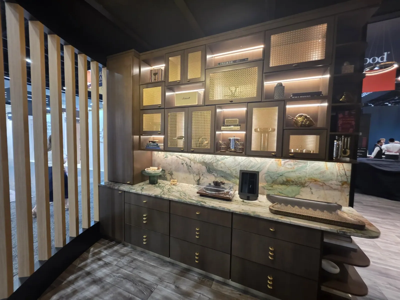 Fabuwood cabinetry room setting with a lit wall of framed material displays above a marble-patterned counter and dark lower cabinets.