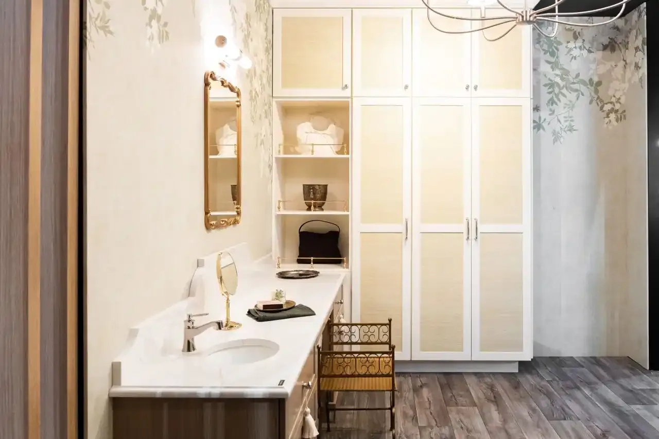 Fabuwood bathroom room setting with white paneled cabinetry, brass-colored fittings, a countertop basin and botanical wall covering.