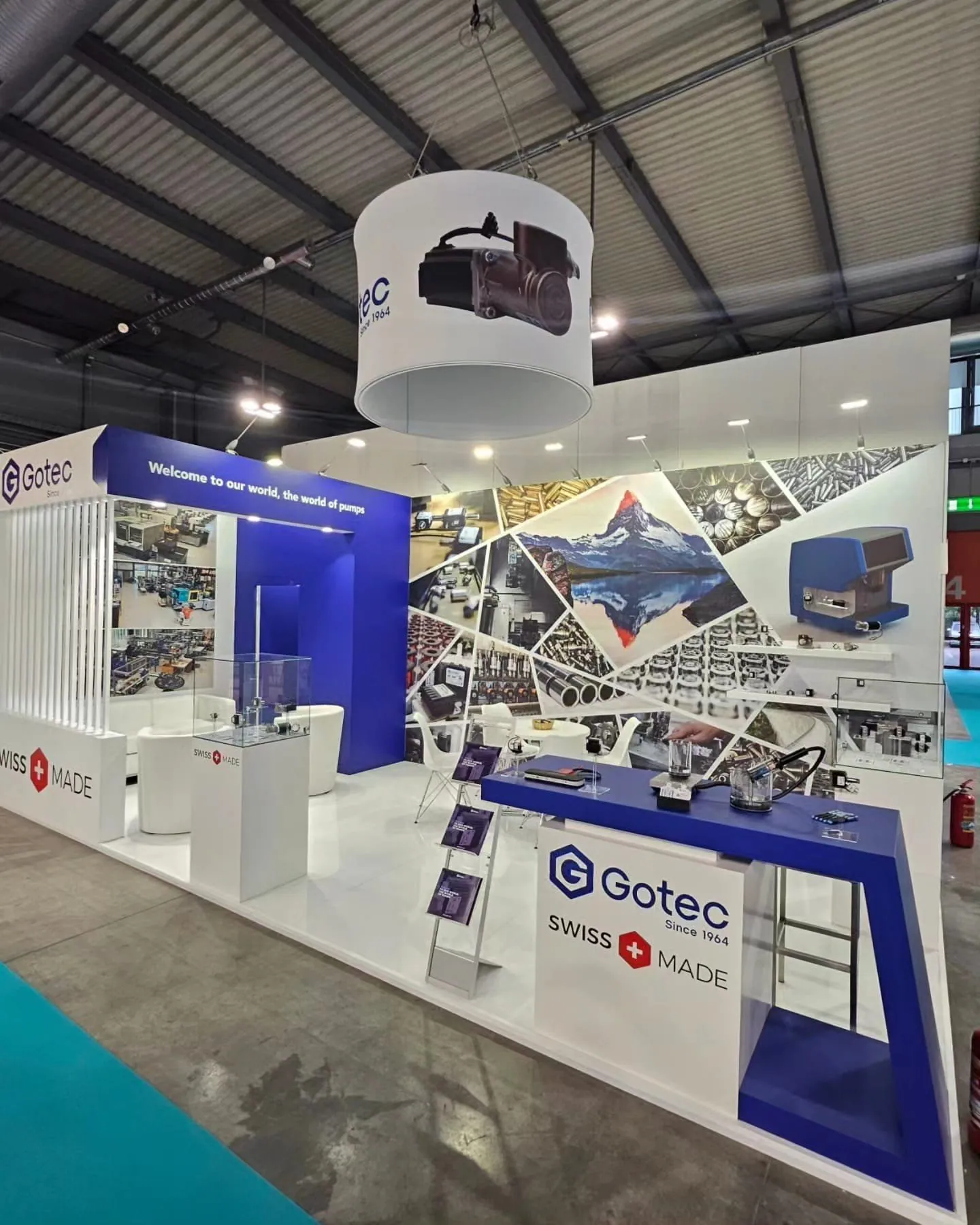 GOTEC exhibit with a blue-and-white counter, pump components, a glass display case, suspended product sign and Swiss manufacturing graphics.
