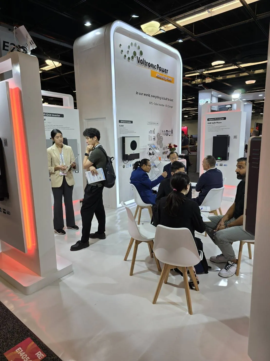 Visitors meeting and discussing products in Voltronic Power’s white exhibit surrounded by solar-inverter displays and orange accent lighting.