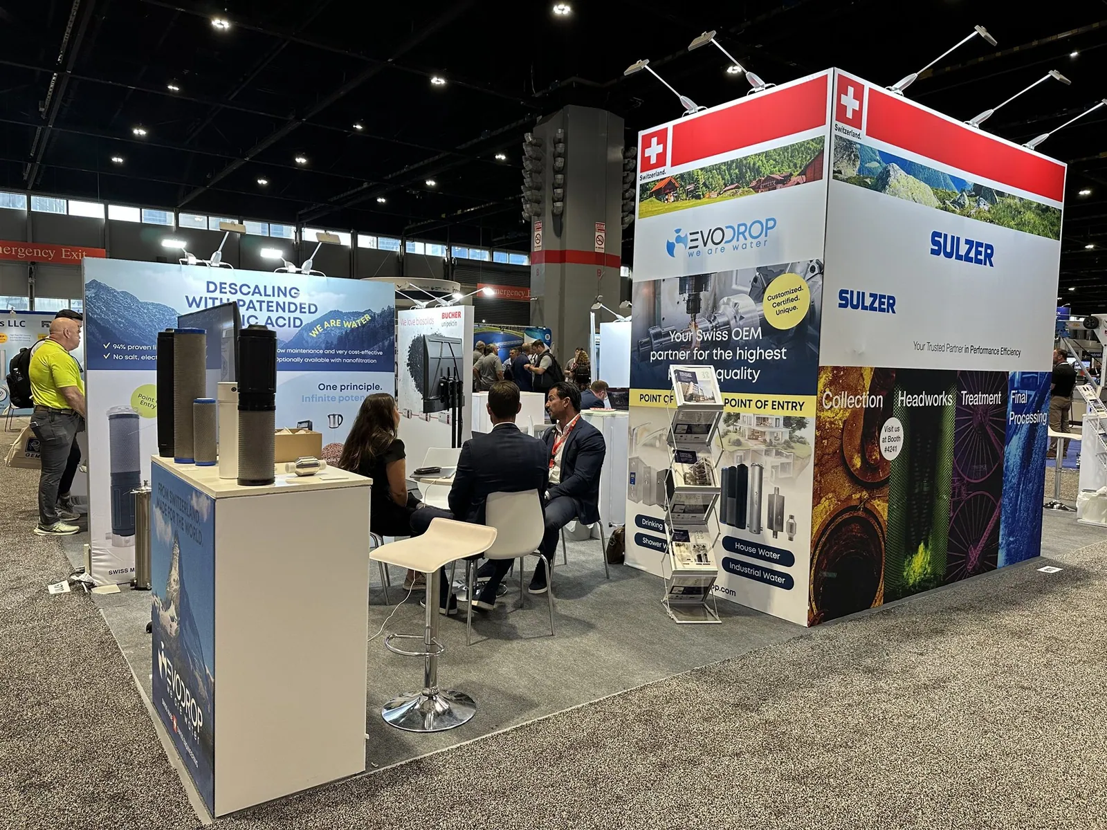 Swiss water-technology pavilion with Evodrop filtration products, Sulzer and Bucher Unipektin branding, sample counters and a seated visitor meeting.