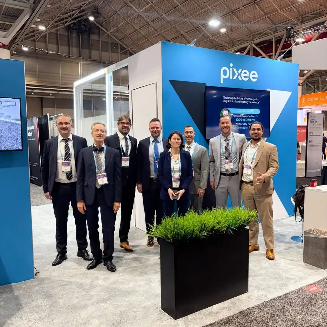 Pixee Medical team standing inside a blue-and-white medical technology booth beside a demonstration screen and glass meeting space.
