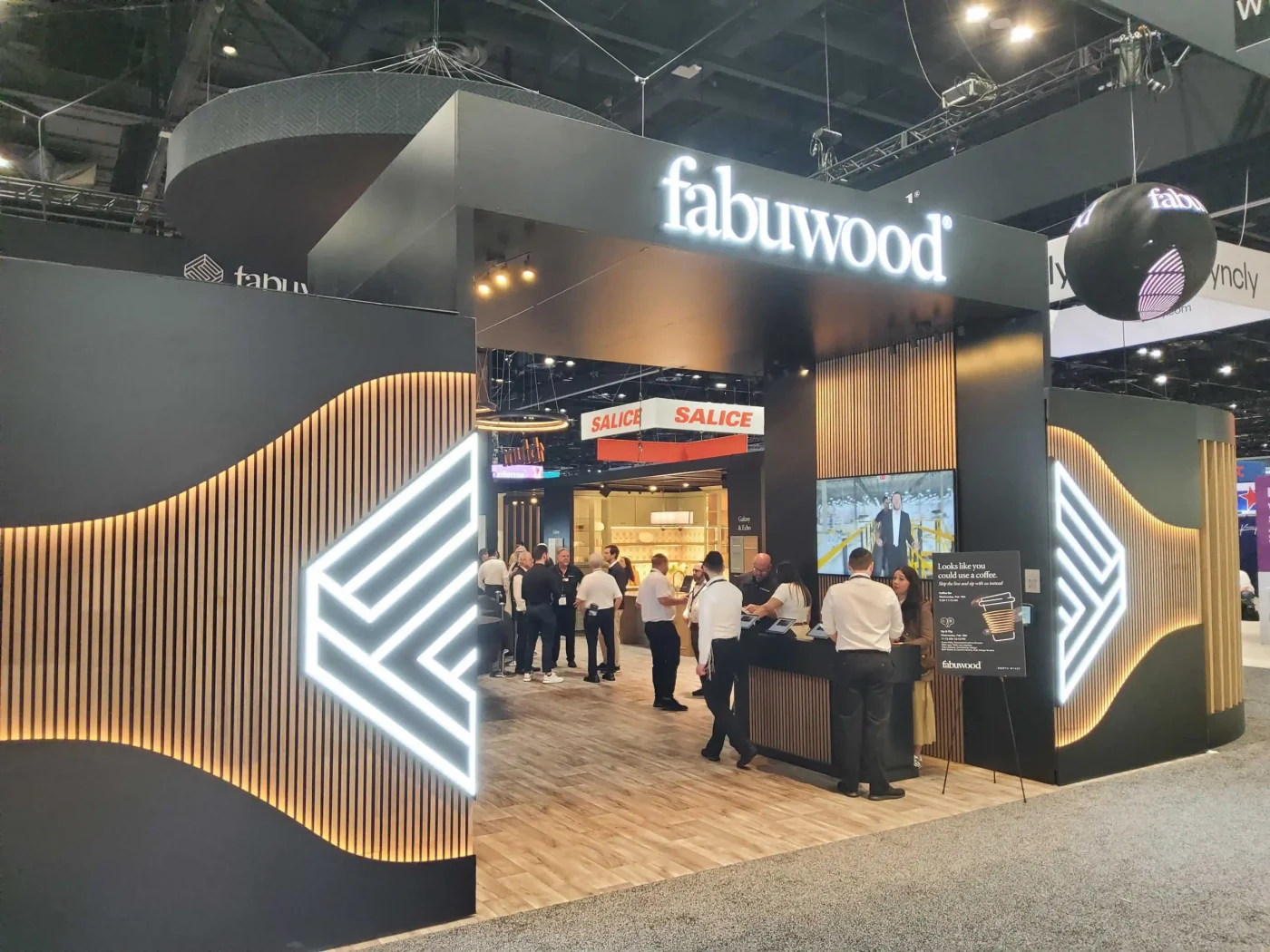 Fabuwood exhibit at KBIS with a large illuminated brand portal, warm timber slat walls and visitors entering the cabinetry displays.
