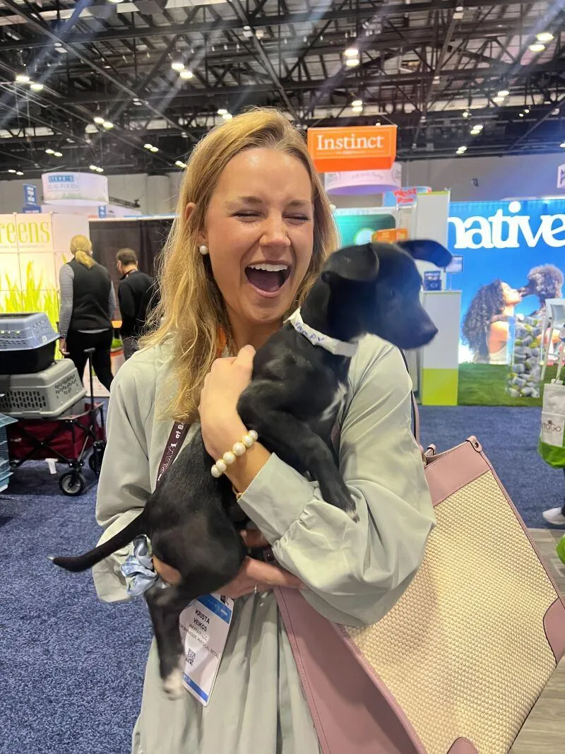 Attractive adult brand ambassadors posing with a dog inside a pet industry exhibit booth at Global Pet Expo.