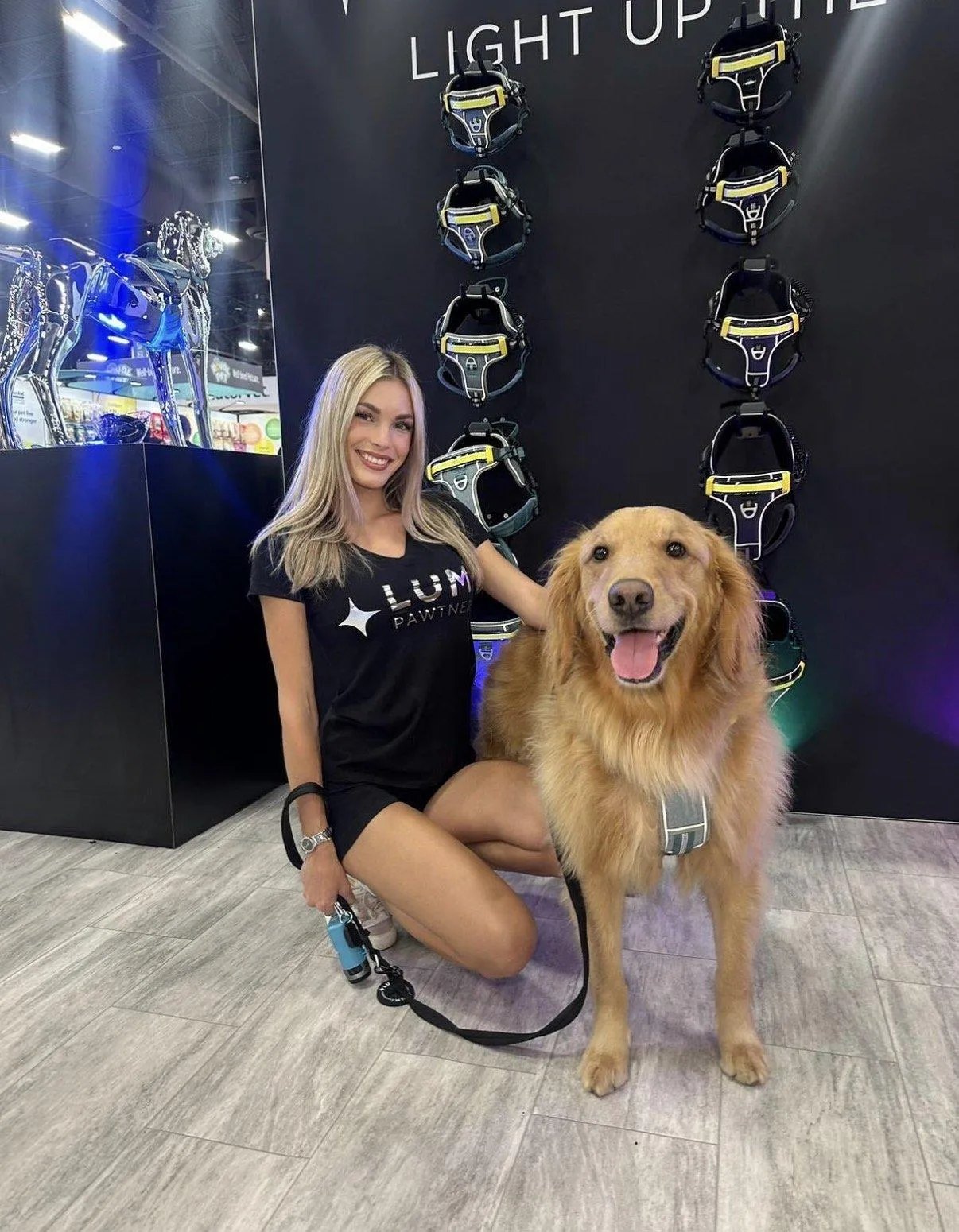 Glamorous adult brand representatives posing with a dog inside a busy exhibit booth at Global Pet Expo.