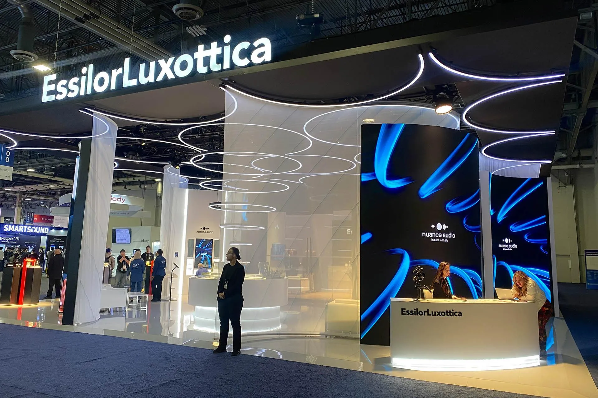 Large custom island booth with illuminated overhead branding and integrated AV displays at Vision Expo