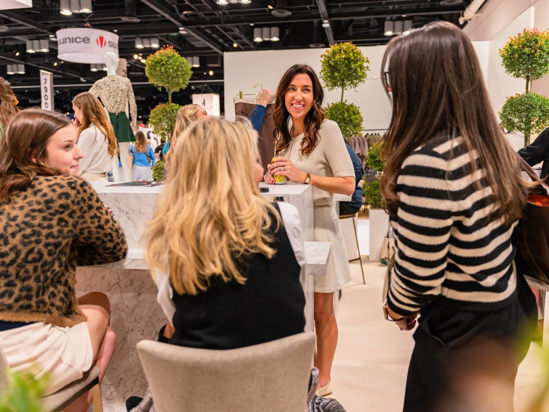 Professional women interacting around a marble display table inside a premium fashion exhibit at the PGA Show in Orlando