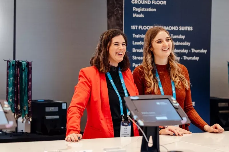 Professional female trade show hostesses welcoming attendees and managing visitor registration at a corporate event